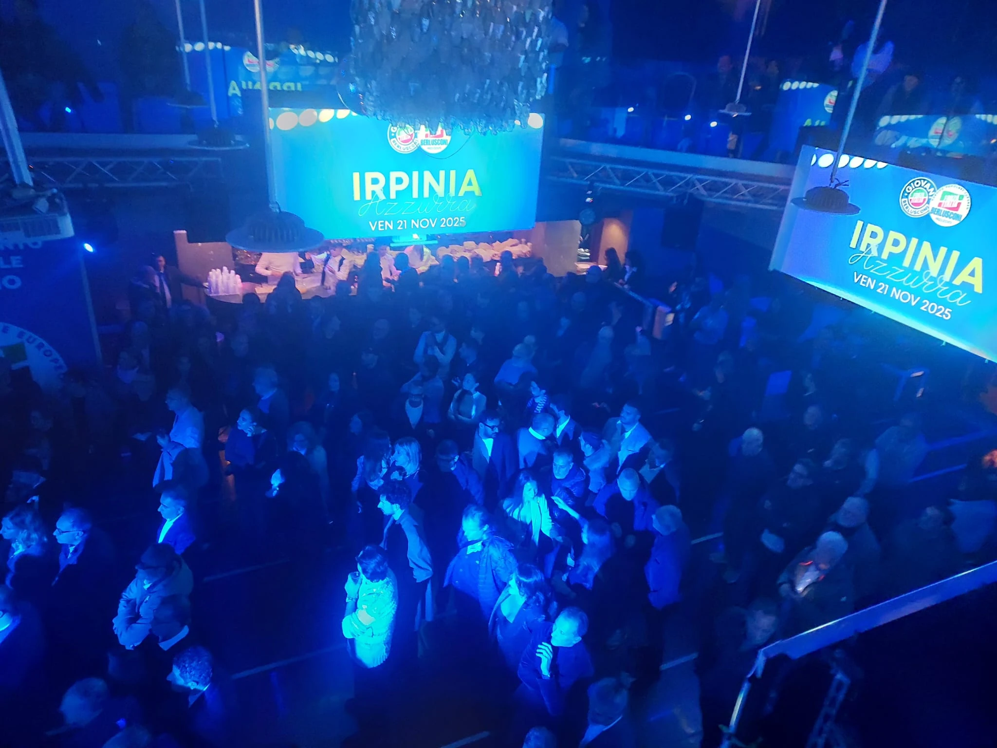 Veduta del pubblico e del palco durante un evento con luci blu. Archivio fotografico Regionali 2025.