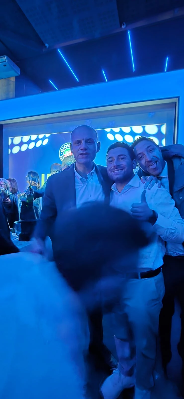 Un momento di incontro e saluto tra i partecipanti in una sala illuminata in blu. Archivio fotografico Regionali 2025.