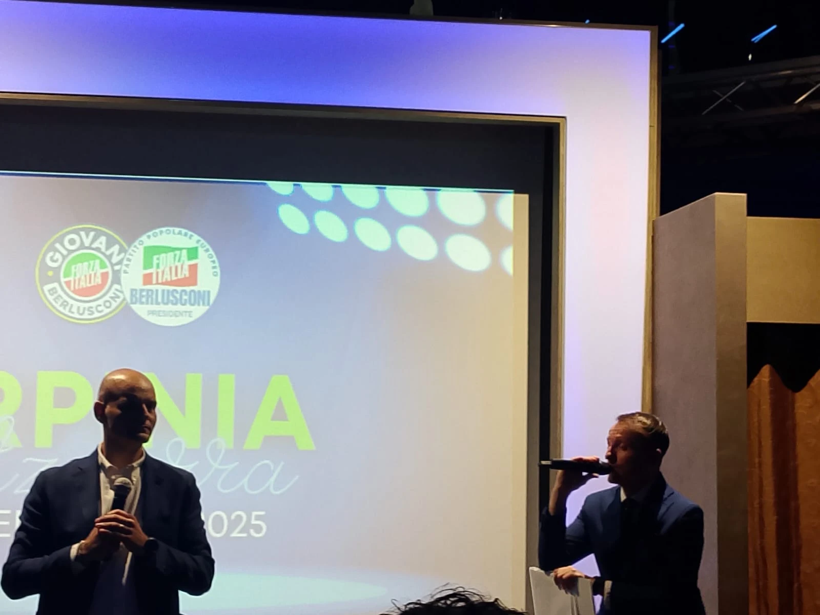 Un intervento al microfono davanti allo schermo di un evento. Archivio fotografico Regionali 2025.